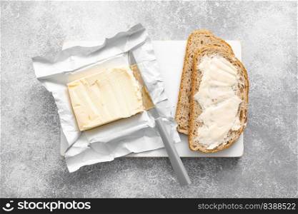 Block of butter with butter knife in a open pack.  Buttering bread