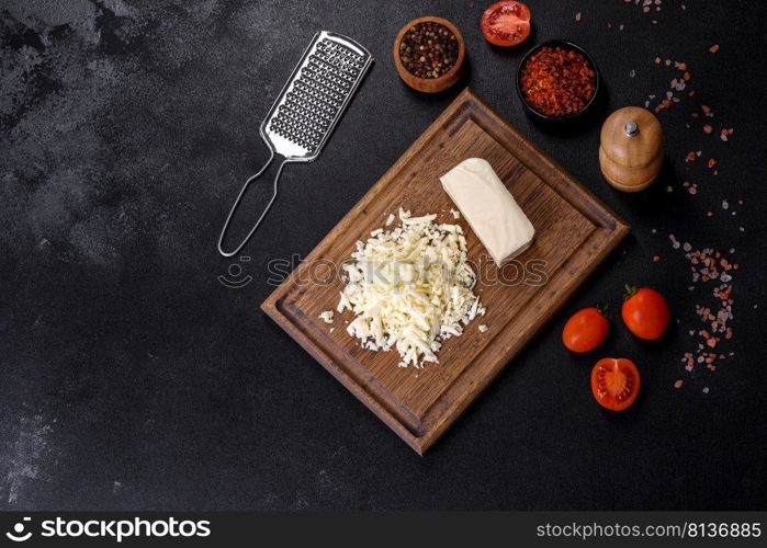 Block of mozzarella cheese and pieces on wooden cutting board. Image of a bar and grated mozzarella cheese on a dark background