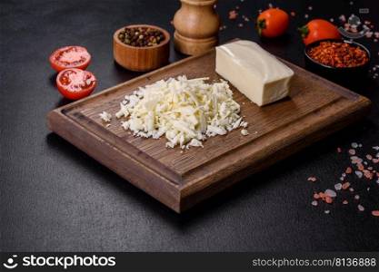 Block of mozzarella cheese and pieces on wooden cutting board. Image of a bar and grated mozzarella cheese on a dark background
