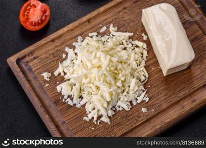 Block of mozzarella cheese and pieces on wooden cutting board. Image of a bar and grated mozzarella cheese on a dark background