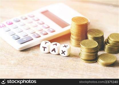 Block word tax on money and calculator on wooden background, TAX on stacked coins financial Tax concept.
