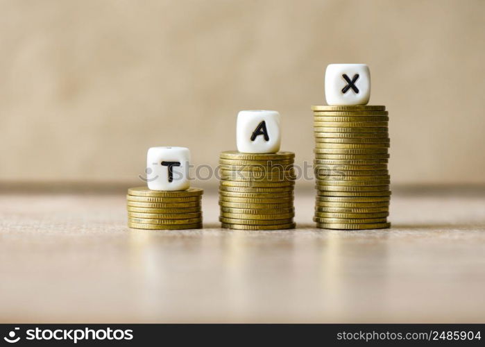 Block word tax on money on wooden background, TAX on stacked coins financial Tax concept.