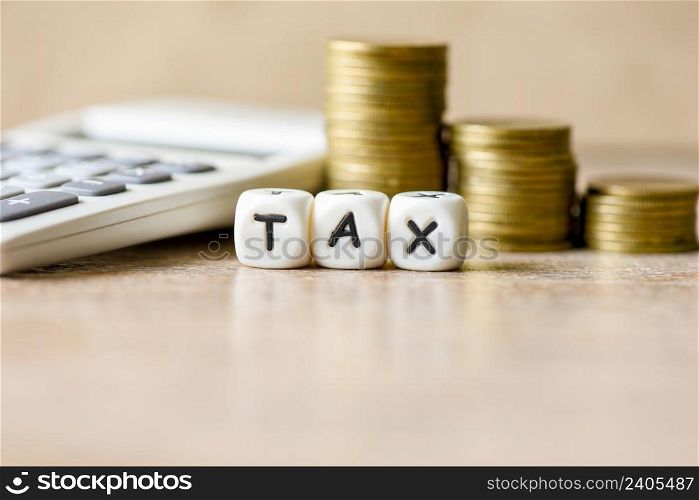 Block word tax with money and calculator on wooden background, TAX and stacked coins financial Tax concept.