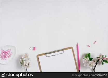 Blogger’s workplace  a tablet with a clip and a sheet of white paper, a pencil and apple flowers on a white background with copy space. Flat lay