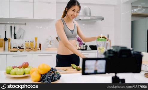 Blogger sporty Asian woman using camera recording how to make apple juice video for her subscriber, female use organic fruit making apple juice by herself at home. Healthy food concept.