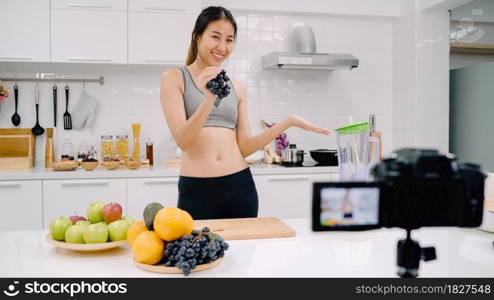 Blogger sporty Asian woman using camera recording how to make grape juice video for her subscriber, female use organic fruit making grape juice by herself at home. Healthy food concept.