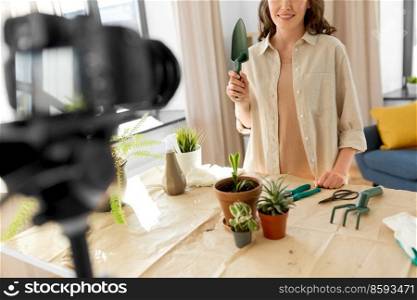 blogging, gardening and housework concept - happy woman or blogger with camera and trowel planting pot flowers and recording tutorial video at home. happy woman or blogger planting flowers at home