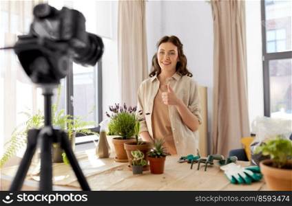 blogging, gardening and housework concept - happy woman or blogger with camera and pot flowers recording tutorial video and showing thumbs up at home. happy woman or blogger planting flowers at home
