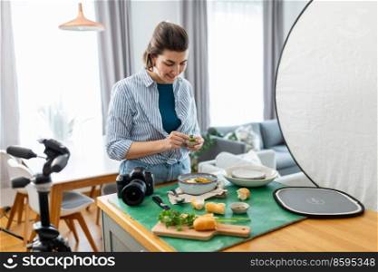 blogging, photographing and people concept - happy smiling female food photographer with camera arranging composition in kitchen at home. food photographer with camera working in kitchen