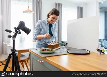 blogging, photographing and people concept - happy smiling female photographer or food blogger with camera, cake and brush working in kitchen at home. food blogger with camera working cake in kitchen