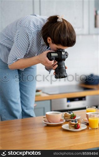 blogging, profession and people concept - female food photographer with camera photographing pancakes, coffee and orange juice in kitchen at home. food photographer with camera working in kitchen