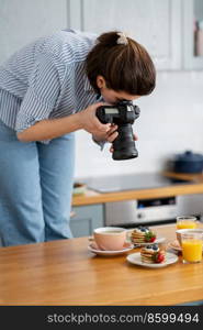 blogging, profession and people concept - female food photographer with camera photographing pancakes, coffee and orange juice in kitchen at home. food photographer with camera working in kitchen