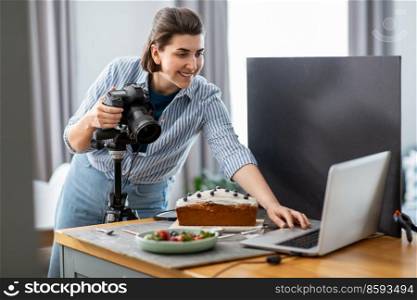 blogging, profession and people concept - happy smiling female food photographer with laptop computer and camera photographing cake in kitchen at home. food photographer with camera working in kitchen