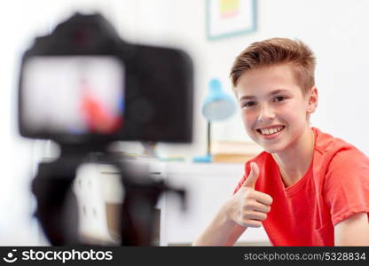 blogging, technology and people concept - happy smiling boy or blogger with camera recording video at home and showing thumbs up. happy boy with camera recording video at home
