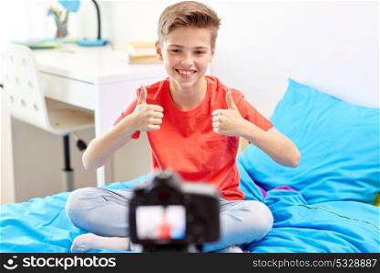 blogging, technology and people concept - happy smiling boy or blogger with camera recording video at home and showing thumbs up. happy boy with camera recording video at home