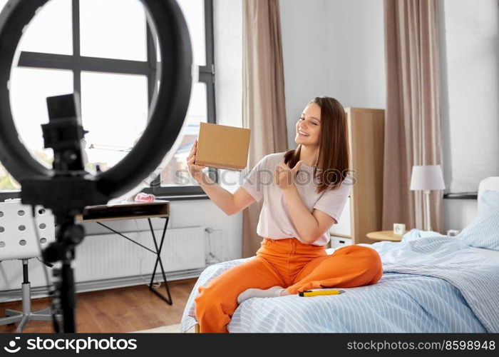 blogging, technology and people concept - happy smiling girl blogger with ring light , smartphone and parcel box showing thumbs up at home. happy girl blogger unpacking parcel box at home