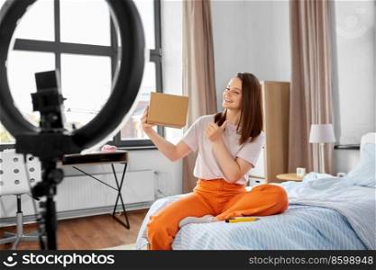 blogging, technology and people concept - happy smiling girl blogger with ring light , smartphone and parcel box showing thumbs up at home. happy girl blogger unpacking parcel box at home