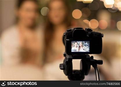 blogging, technology, hygge and pajama party concept - happy female friends or teenage bloggers with camera recording video at home. female bloggers with camera recording home video