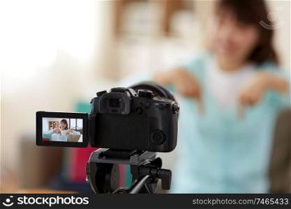 blogging, technology, videoblog and shopping concept - camera recording video blog of happy smiling asian woman or blogger pointing fingers downwards at home. female blogger making video blog about shopping