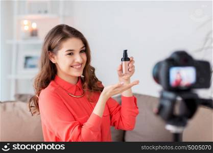 blogging, technology, videoblog, makeup and people concept - happy smiling woman or beauty blogger with foundation and camera recording tutorial video at home. woman with foundation and camera recording video