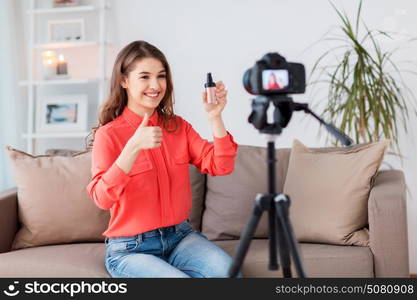 blogging, technology, videoblog, makeup and people concept - happy smiling woman or beauty blogger with foundation and camera recording tutorial video at home and showing thumbs up. woman with foundation and camera recording video