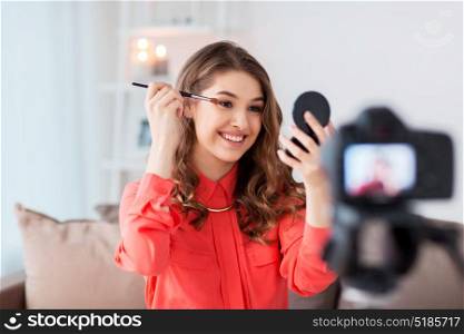 blogging, technology, videoblog, makeup and people concept - happy smiling woman or beauty blogger with eye shadow brush, mirror and camera recording makeup tutorial video at home. woman recording eye makeup tutorial video at home