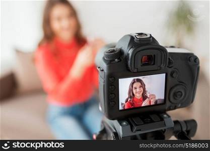 blogging, technology, videoblog, makeup and people concept - happy smiling woman or beauty blogger with lipstick and camera recording tutorial video at home. woman with lipstick and camera recording video
