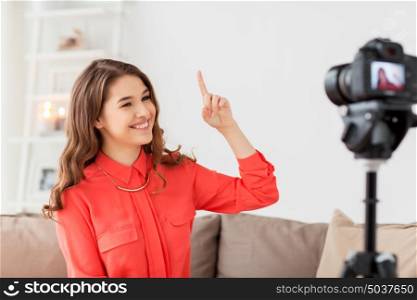 blogging, technology, videoblog, mass media and people concept - happy smiling woman or blogger with camera recording video at home and pointing finger up. woman with camera recording video at home