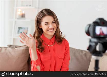 blogging, technology, videoblog, mass media and people concept - happy smiling young woman or blogger with camera recording video and waving hand at home. happy woman with camera recording video at home