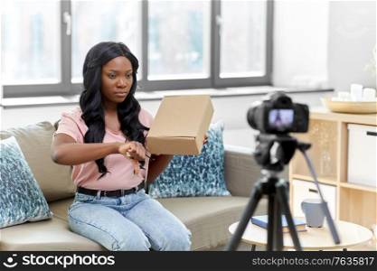blogging, videoblog and people concept - african american female video blogger with parcel box and camera videoblogging at home. female video blogger with camera and box at home