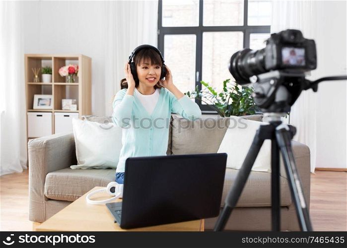 blogging, videoblog and people concept - asian female blogger with camera and laptop computer recording video review of headphones at home. female blogger with headphones making video blog