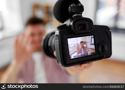blogging, videoblog and people concept - close up of camera recording smiling male video blogger waving hand at home office. close up of camera recording male video blogger