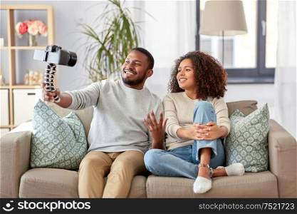 blogging, videoblog and people concept - happy african american couple of video bloggers with camera videoblogging at home. couple of video bloggers with camera at home