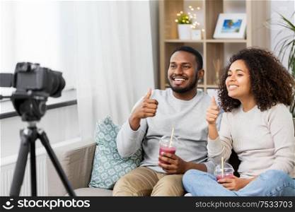 blogging, videoblog and people concept - happy african american couple of video bloggers with camera and smoothie drinks videoblogging at home. couple of video bloggers with camera at home