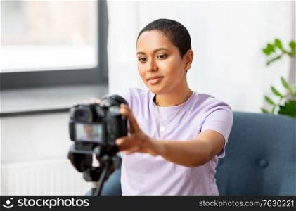 blogging, videoblog and people concept - happy african american female video blogger adjusting camera on tripod at home. female video blogger adjusting camera at home