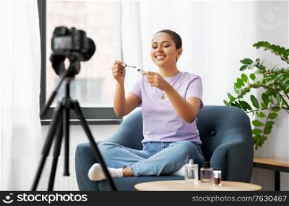 blogging, videoblog and people concept - happy smiling african american female beauty blogger with camera and make up cosmetics videoblogging at home. female beauty blogger with camera and mascara