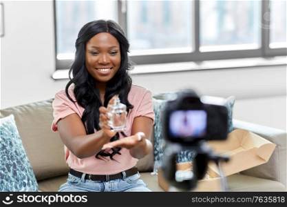 blogging, videoblog and people concept - happy smiling african american female beauty blogger with camera and perfume videoblogging at home. female beauty blogger with camera and perfume