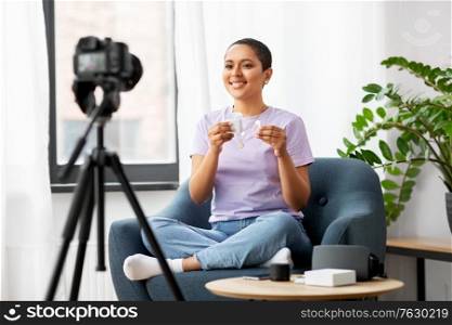 blogging, videoblog and people concept - happy smiling african american female video blogger with camera and wireless earphones videoblogging at home. female blogger with camera video blogging at home