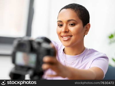 blogging, videoblog and people concept - happy smiling african american female video blogger adjusting camera at home. female video blogger adjusting camera at home