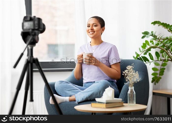 blogging, videoblog and people concept - happy smiling african american female video blogger with camera and cup of coffee videoblogging at home. female blogger with camera and coffee at home