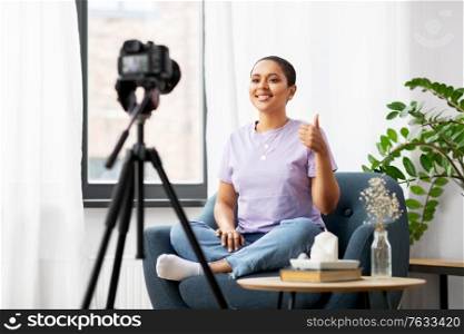 blogging, videoblog and people concept - happy smiling african american female video blogger with camera videoblogging at home and showing thumbs up. female blogger with camera video blogging at home