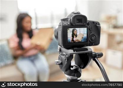 blogging, videoblog and people concept - happy smiling african american female video blogger with parcel box and camera videoblogging at home. female video blogger with camera and box at home