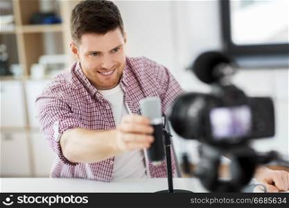 blogging, videoblog and people concept - male blogger with camera recording video review of wireless microphone at home office. male blogger with microphone videoblogging