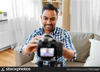 blogging, videoblog and people concept - smiling indian male video blogger adjusting camera at home. indian male video blogger adjusting camera at home