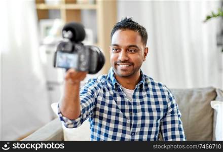 blogging, videoblog and people concept - smiling indian male video blogger with camera videoblogging at home. male video blogger with camera blogging at home