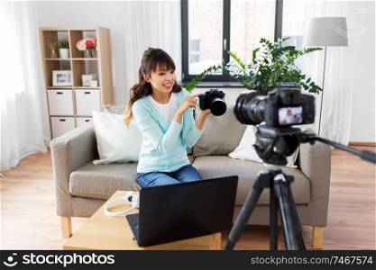 blogging, videoblog and technology concept - asian woman or blogger with photo camera and laptop computer recording video blog at home. asian female blogger with camera recording video