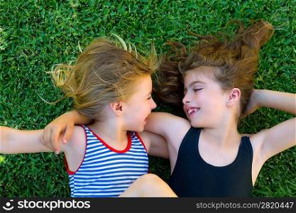 Blond and brunette sisters kid girls smiling lying on garden grass