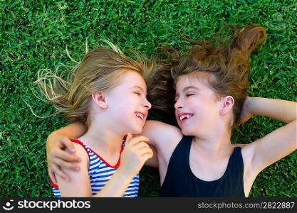 Blond and brunette sisters kid girls smiling lying on garden grass