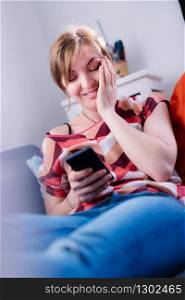 Blond attractive girl is lying on the sofa and texting with her boyfriend