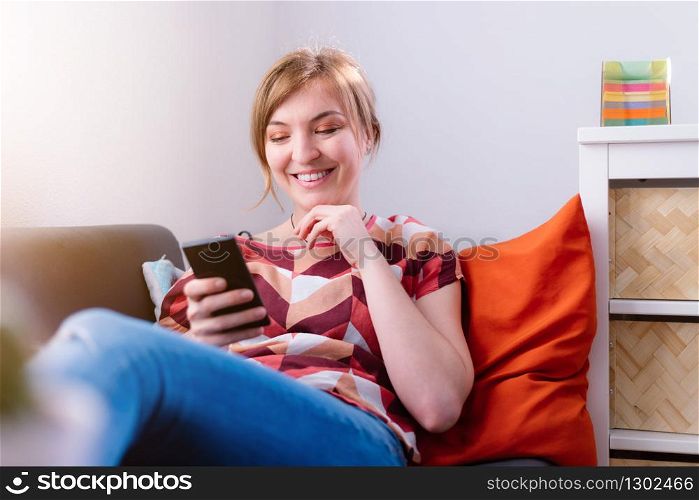 Blond attractive girl is lying on the sofa and texting with her boyfriend